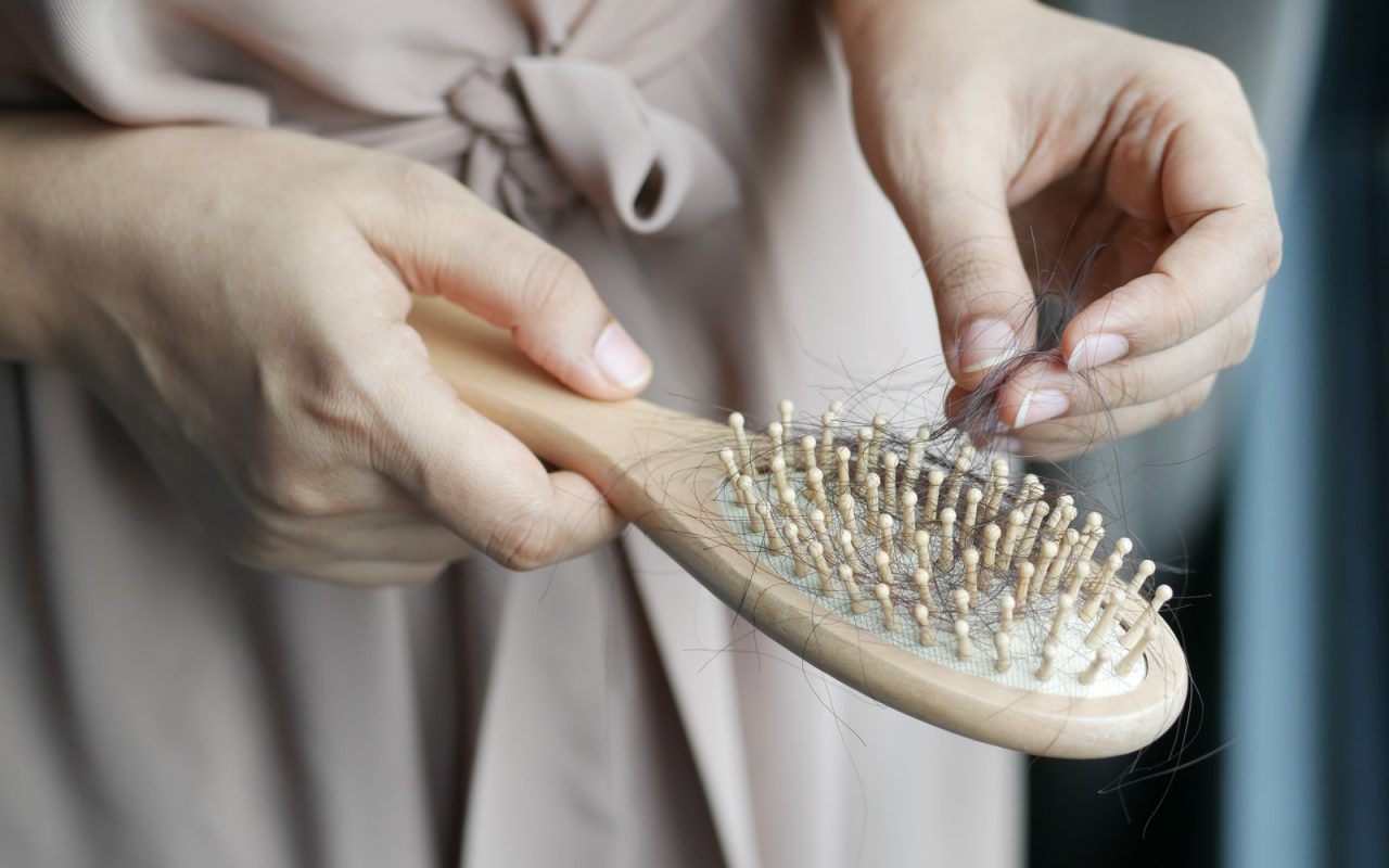 Hands removing shed hair from a wooden hairbrush
