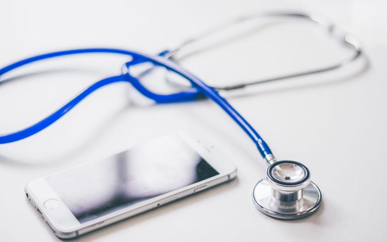 A blue stethoscope beside a smartphone on a white surface