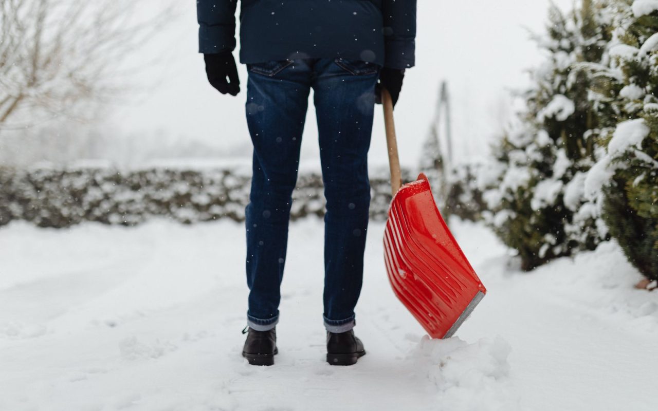 A person shovelling snow with a red shovel during snowfall