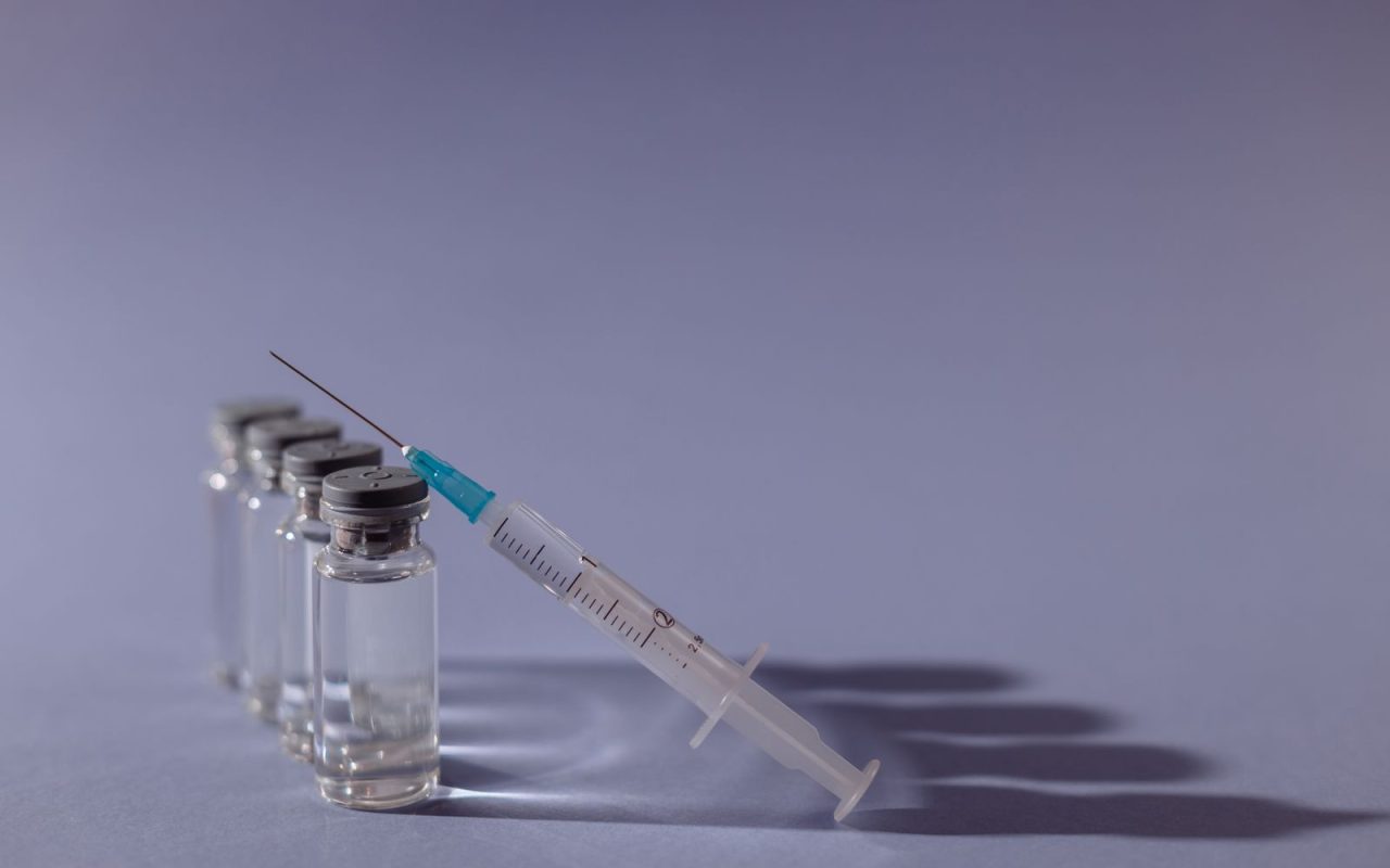 A syringe and vaccine vials on a grey surface