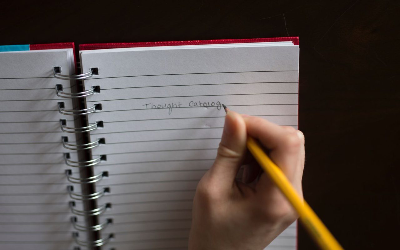 A hand writing in a spiral notebook with a pencil