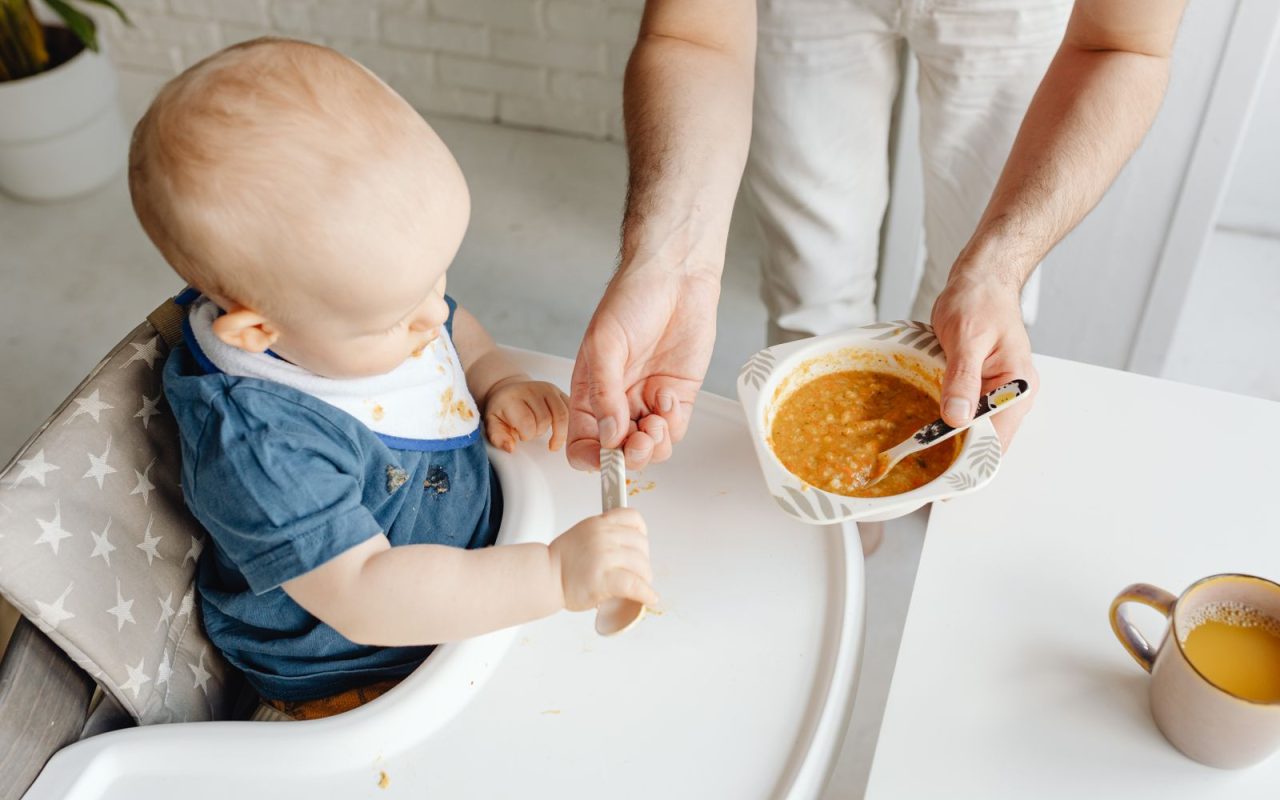 A parent feeding a baby in a high chair
